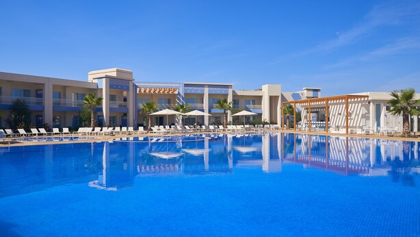 A large swimming pool with lounge chairs and umbrellas, surrounded by a hotel building with multiple floors and balconies. - Radisson Blu Resort, Saidia Garden (Madagh)
