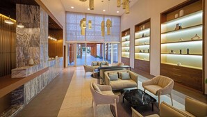 A modern lobby with marble walls, a reception desk, seating area, and illuminated shelves. - Radisson Blu Resort, Saidia Garden (Madagh)