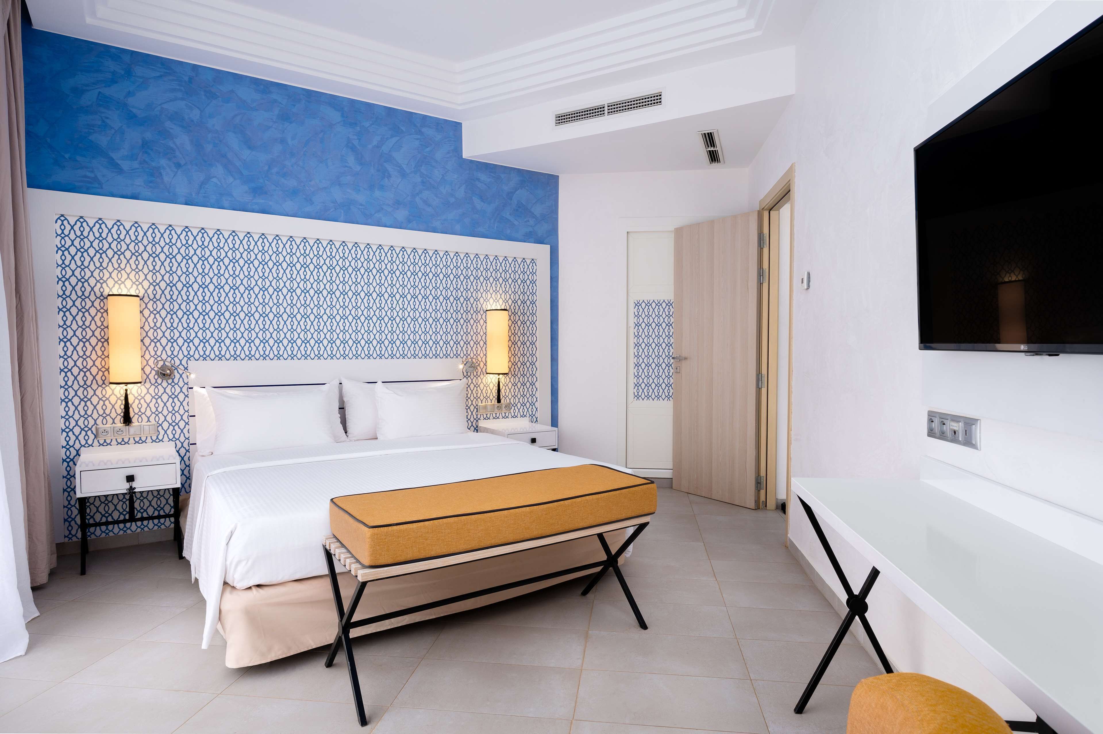 A modern hotel room with a bed, bedside lamps, a TV, and a desk.