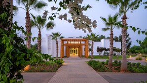 A pathway leading to a building entrance with a wooden pergola, surrounded by palm trees and greenery. - Radisson Blu Resort, Saidia Garden (Madagh)