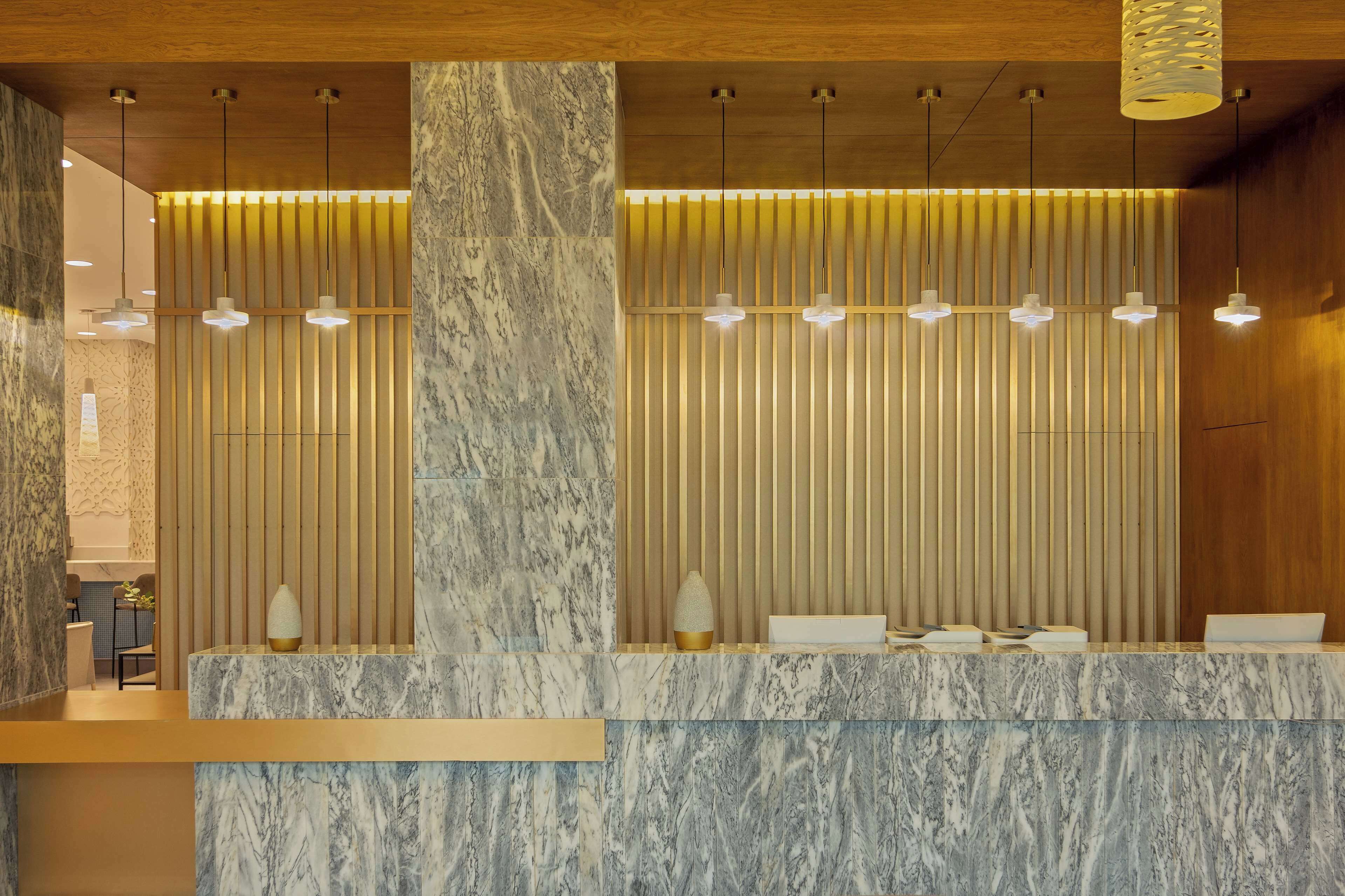 A reception area with marble counters, wooden slats, and pendant lighting.