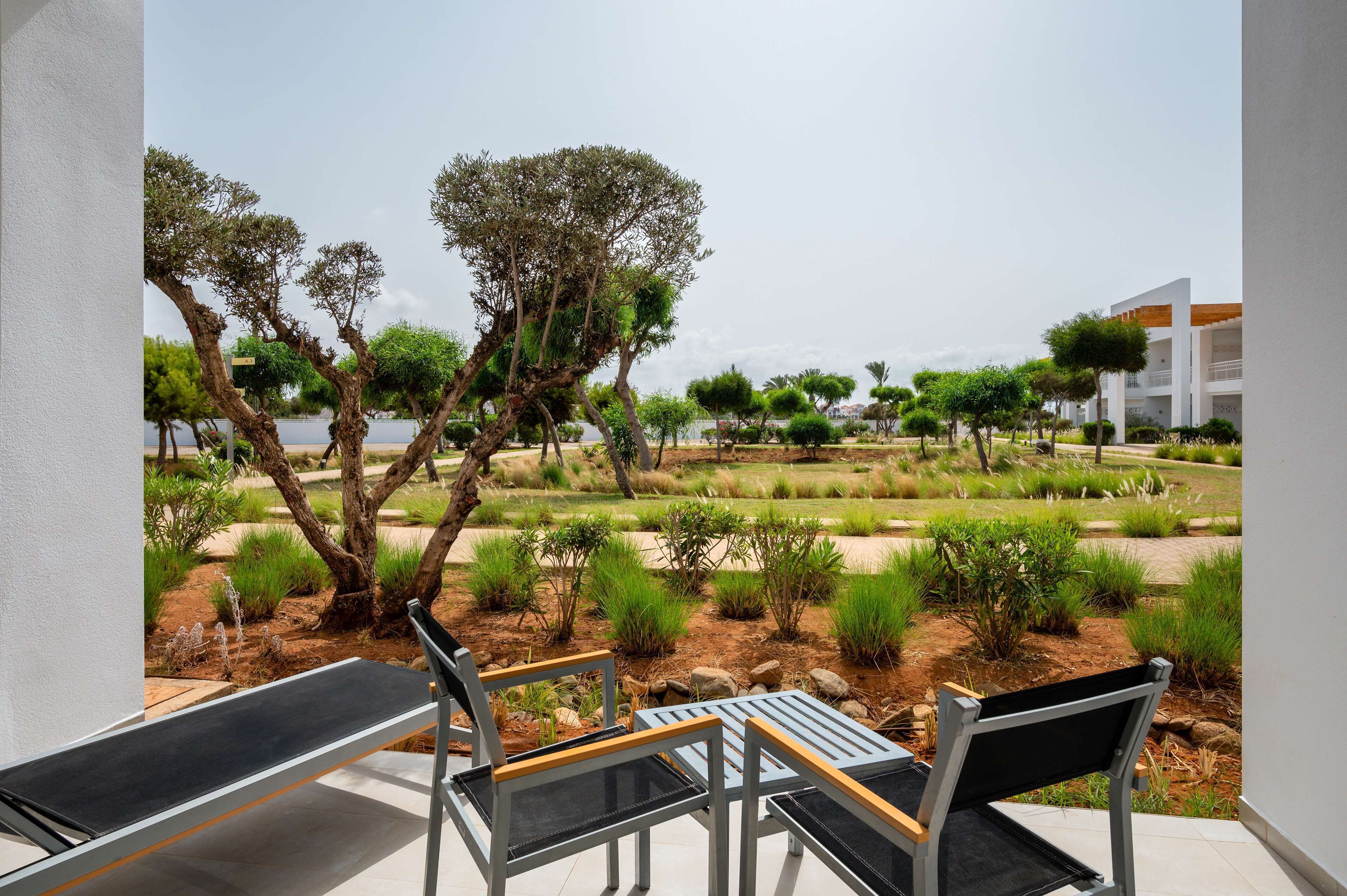 A terrace with outdoor furniture, a view of a landscaped garden, and a modern building in the background.