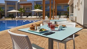 A poolside dining area with tables, chairs, and a buffet table with food and drinks. - Radisson Blu Resort, Saidia Garden (Madagh)