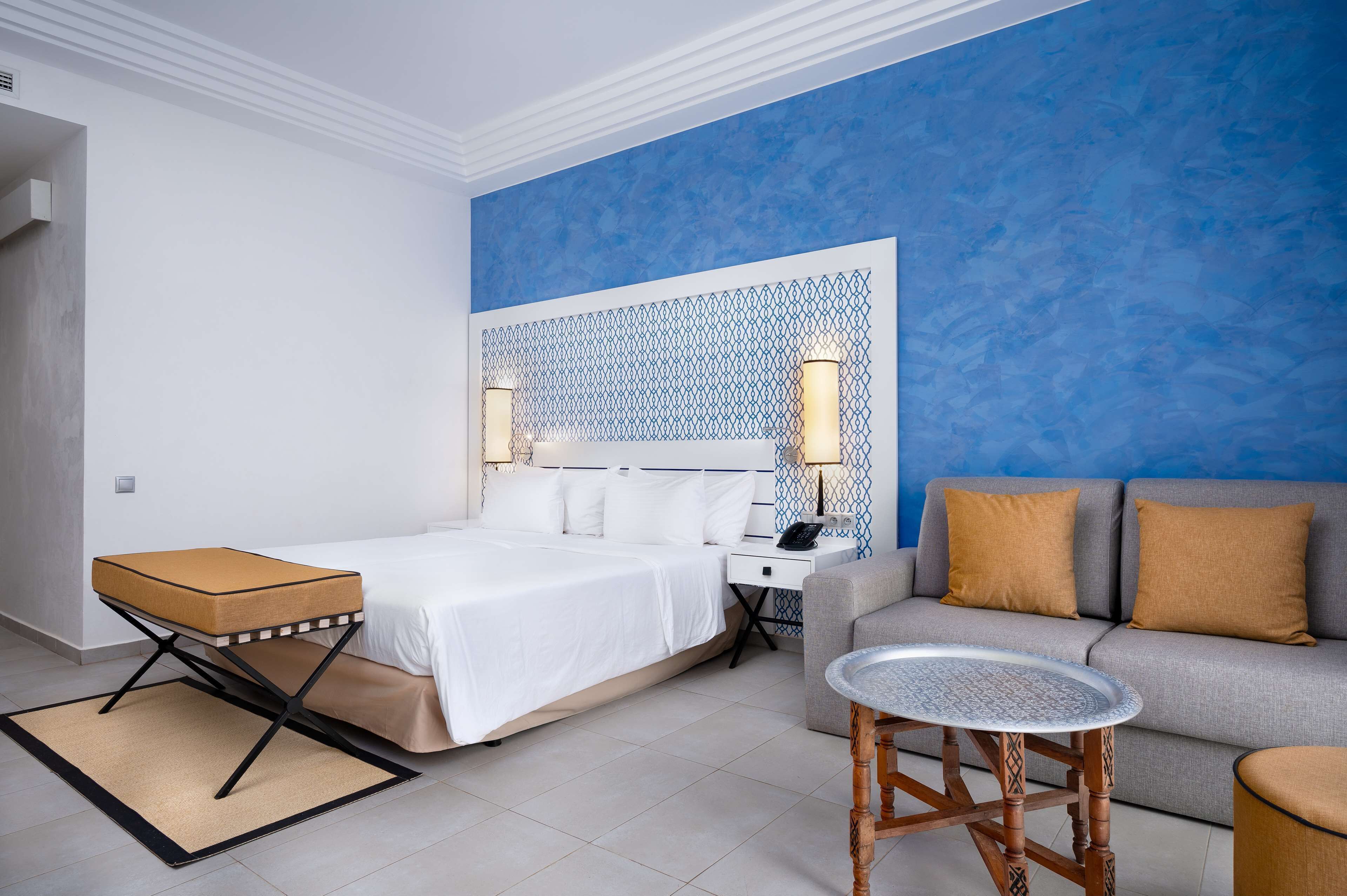 A modern hotel room with a bed, a sofa, a small table, and a decorative wall panel.