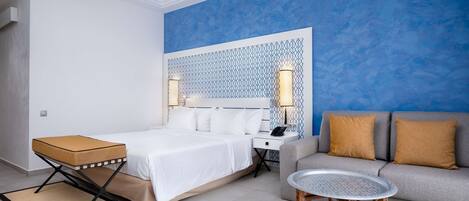 A modern hotel room with a bed, a sofa, a small table, and a decorative wall panel.