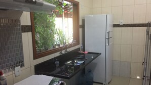 Una pequeña cocina con refrigerador, lavamanos y una ventana con plantas.