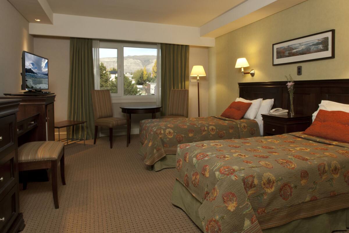 Ein Hotelzimmer mit zwei Betten, einem Schreibtisch, einem Sessel, einem Fernseher und einem Fenster mit Blick.