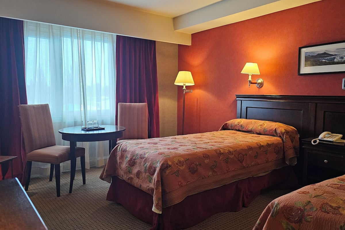 Ein Hotelzimmer mit zwei Betten, einem Schreibtisch, einem Stuhl, einem kleinen Tisch und einer Lampe.