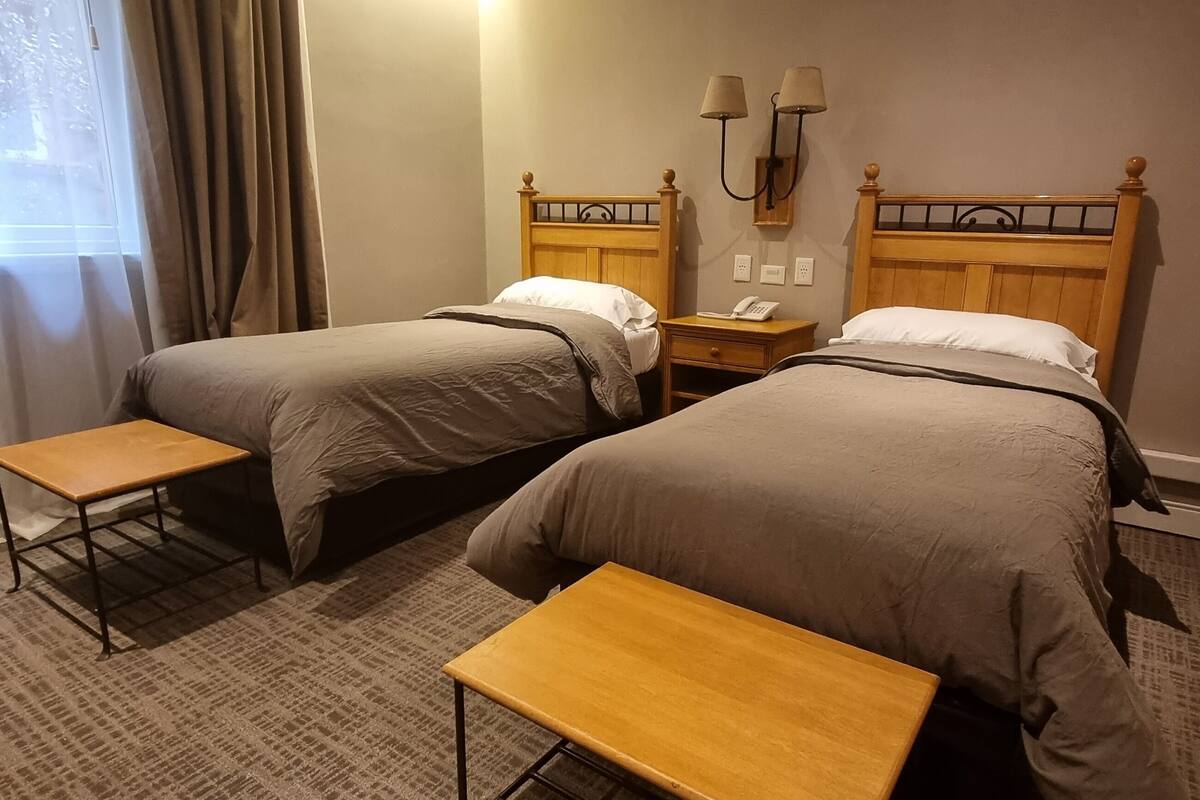 Ein Hotelzimmer mit zwei Einzelbetten, einem Nachttisch mit Lampe und einem kleinen Tisch.