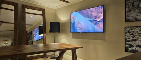 A modern living room with a large flat-screen TV mounted on the wall, a wooden coffee table, and a patterned rug.