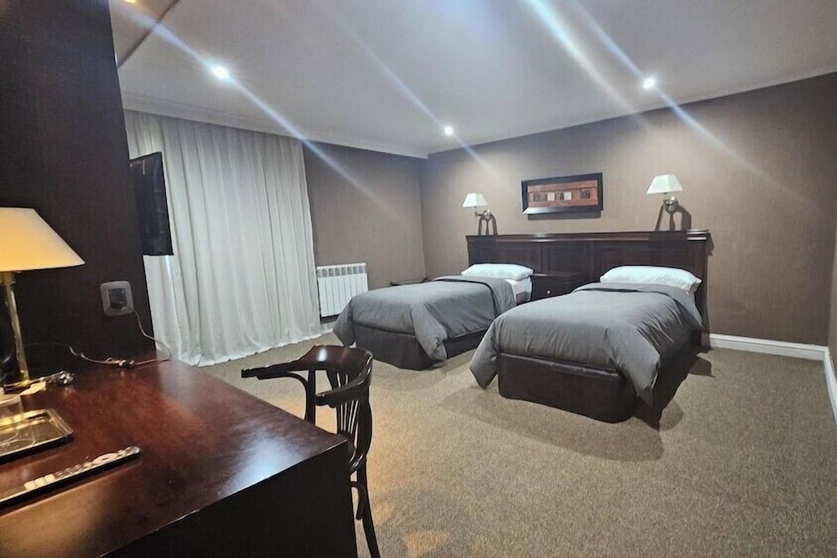 Ein Hotelzimmer mit zwei Betten, einem Schreibtisch mit Lampe, einem Sessel und einer Heizung.
