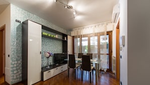 A modern kitchen with a built-in oven, a dining area with a glass table and chairs, and a view through a window with sheer curtains. - Domus Al Parco Guest House (Fiumicino)