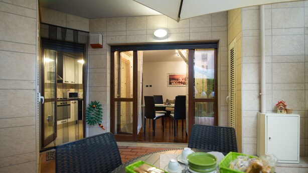 A dining area with a table set for two, a small cabinet, and a sliding glass door leading to a kitchen. - Domus Al Parco Guest House (Fiumicino)