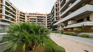 A multi-story residential building with balconies, a paved walkway, and a small palm tree. - Domus Al Parco Guest House (Fiumicino)