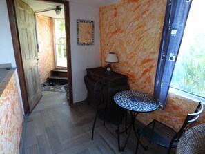 Ein Zimmer mit Fliesenboden, einer Holztür, einem kleinen Tisch mit Lampe und einem Stuhl.