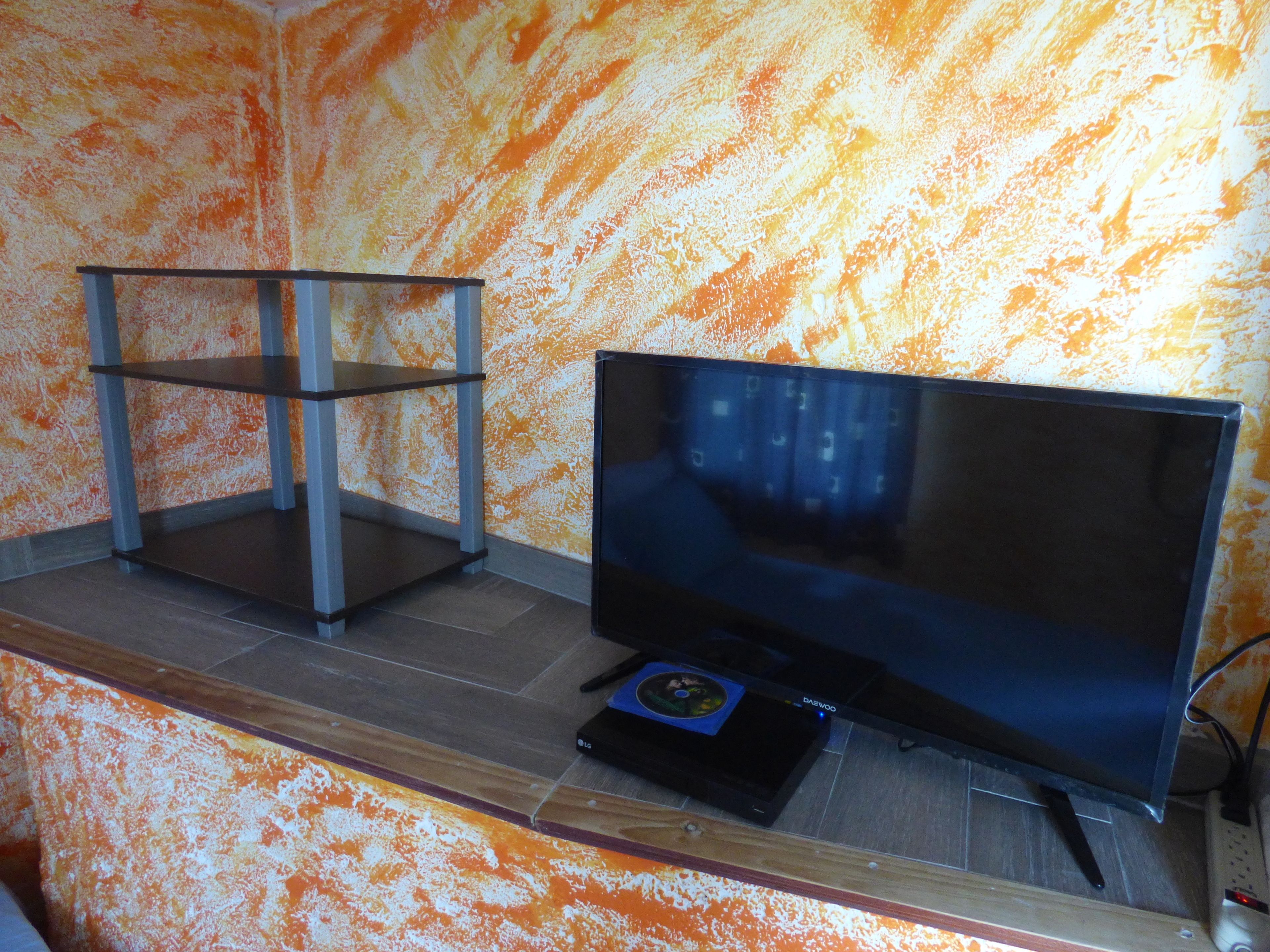 A room with a television on a wooden stand, a small table, and a patterned orange wall.