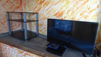 A room with a television on a wooden stand, a small table, and a patterned orange wall.