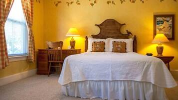 A bedroom with a large bed, two bedside lamps, a wooden chair, and a window with curtains.