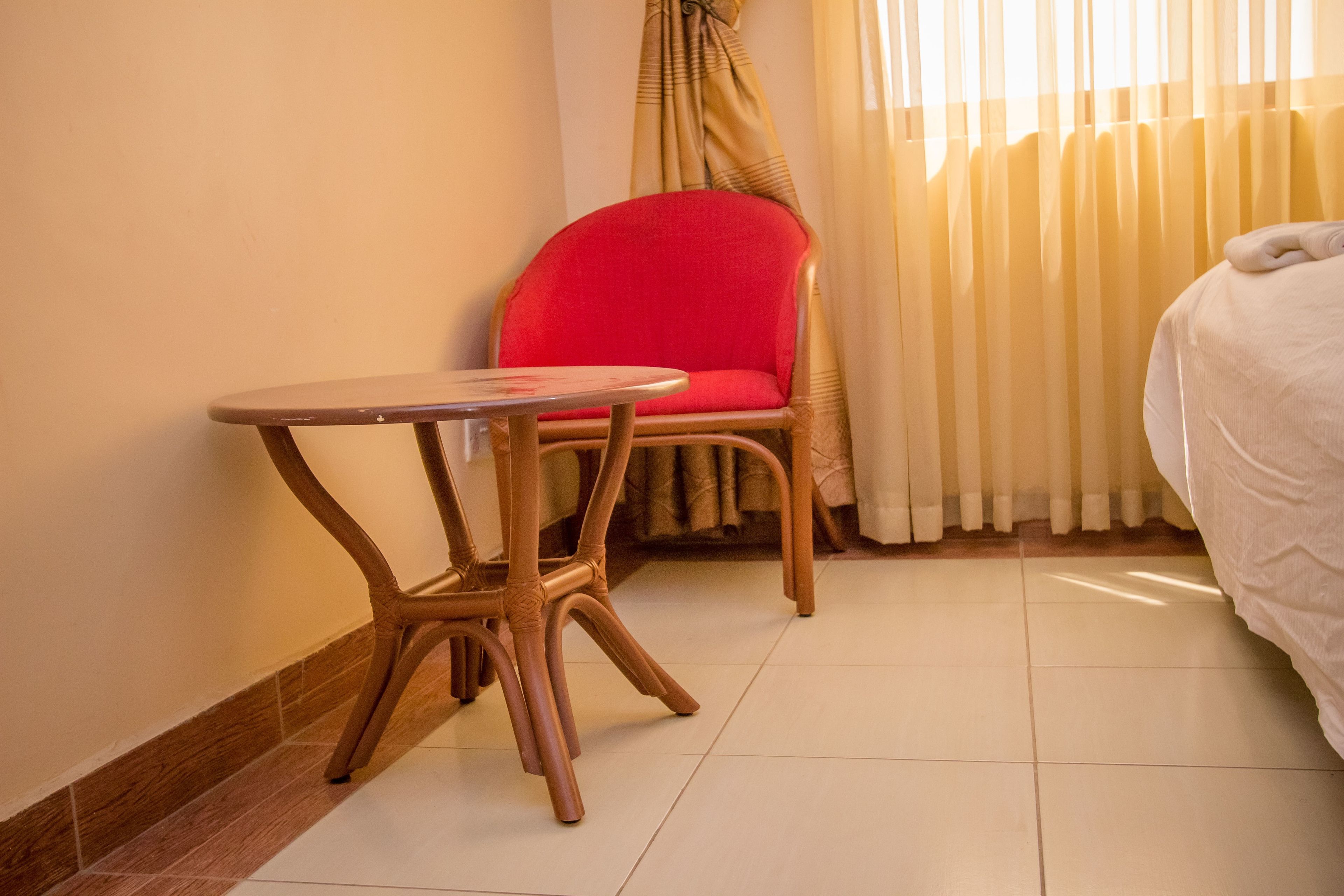 A hotel room with a wooden chair, a small round table, a bed, and a window with curtains.