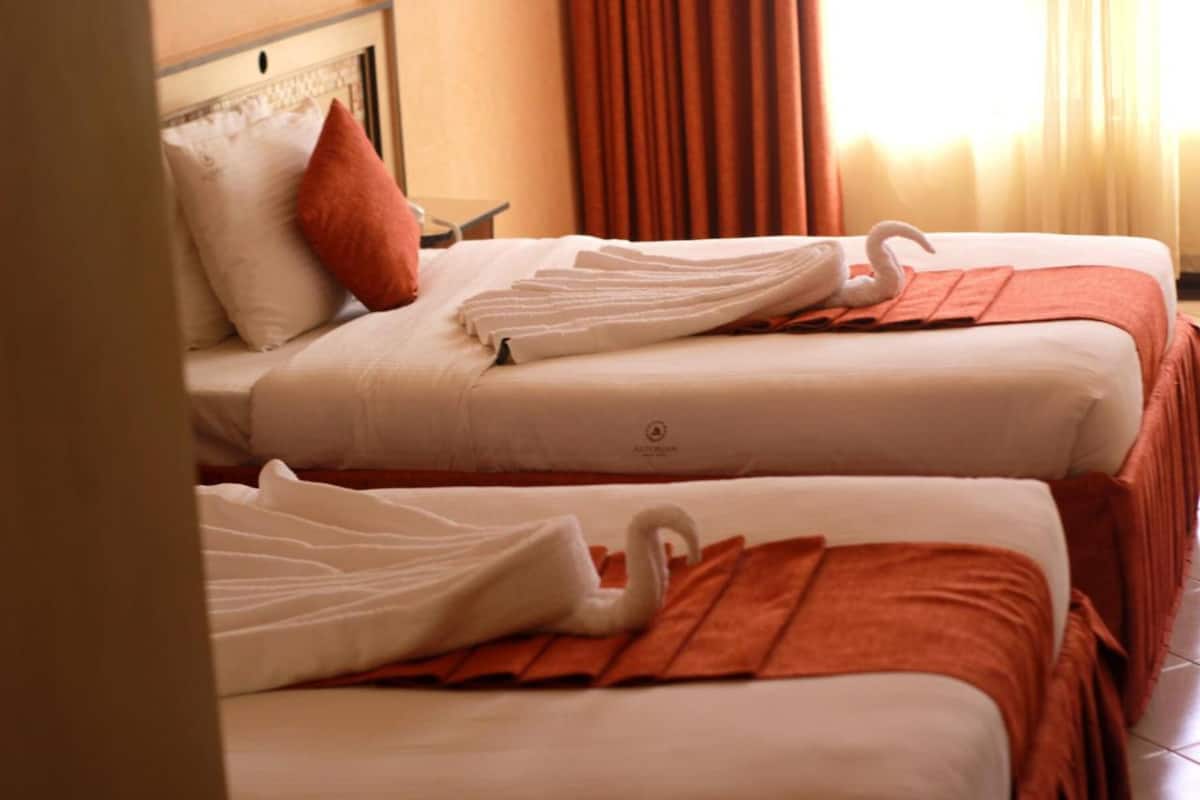 A hotel room with two beds, each with a swan-shaped towel and a red blanket.