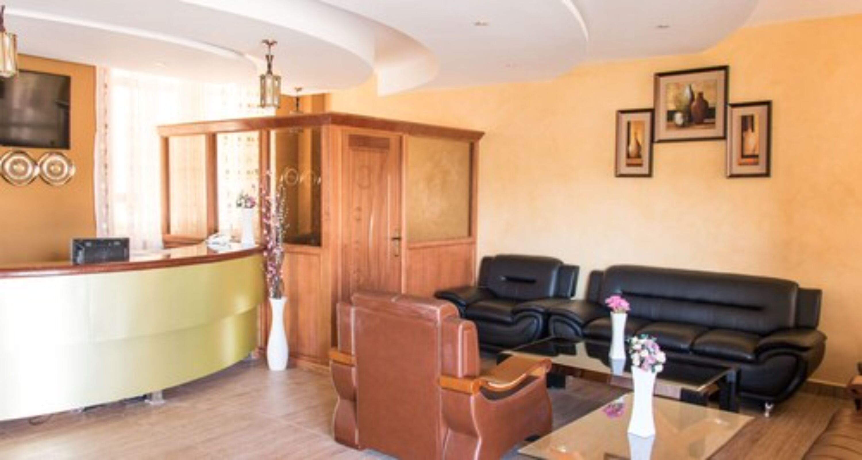 A reception area with a counter, wooden cabinet, leather sofa, and framed pictures on the wall.