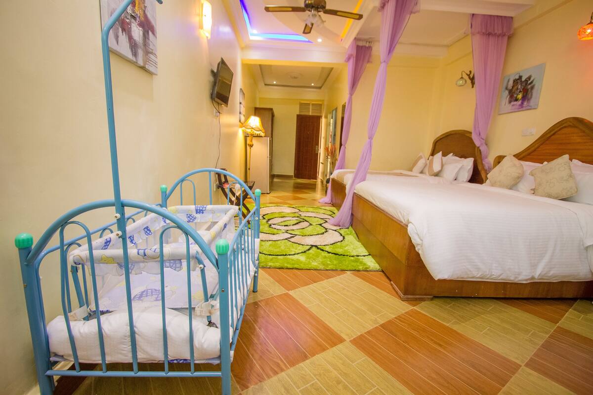 A hotel room with a bed, a crib, a patterned rug, and a ceiling fan.