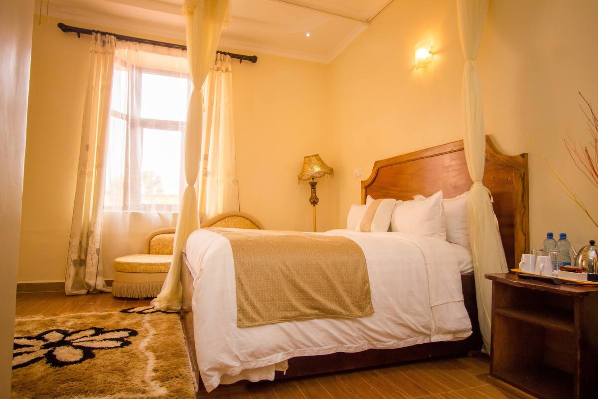 A hotel room with a bed, a bedside table, a lamp, a chair, and a window with curtains.
