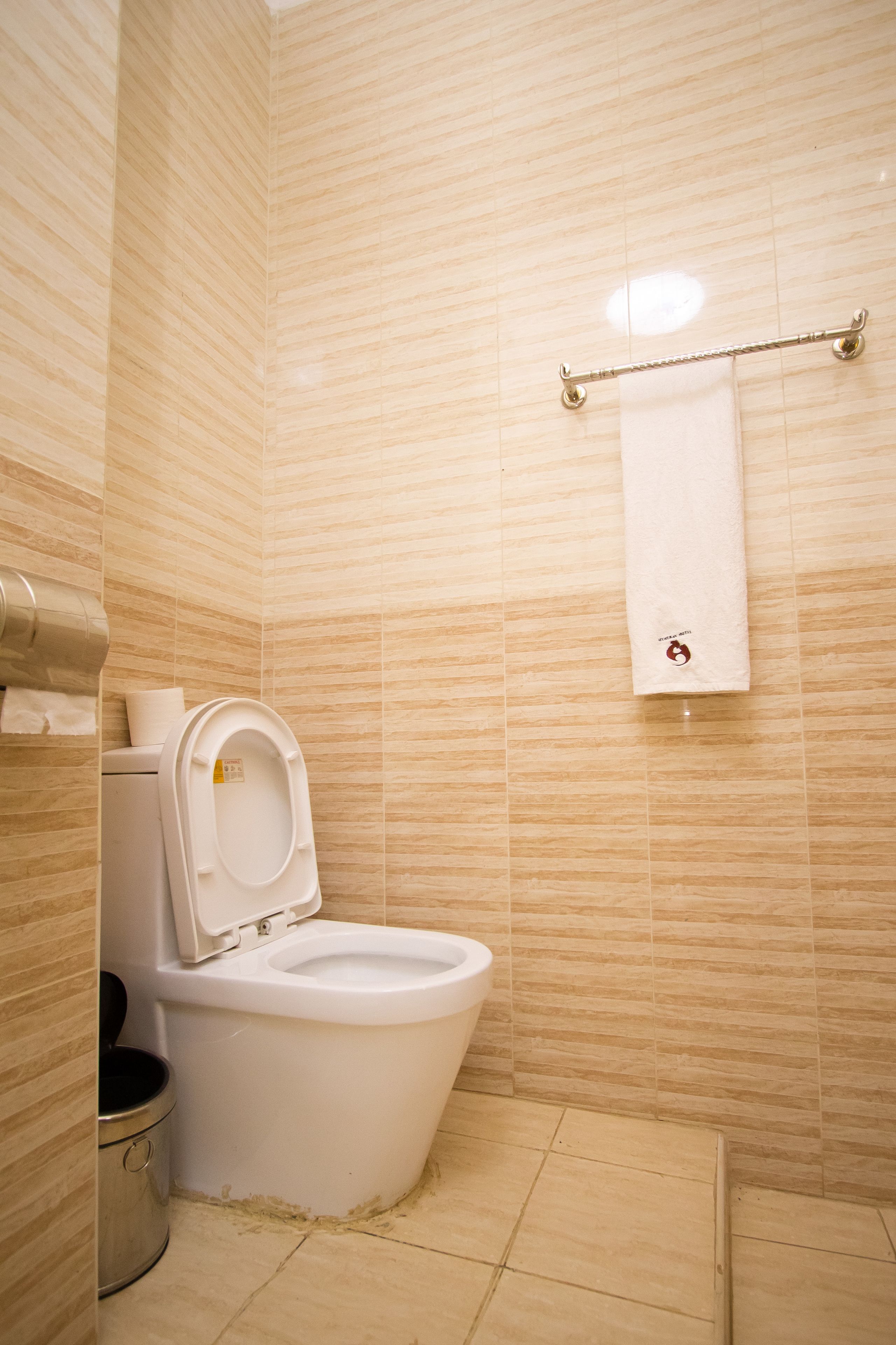 A bathroom with a toilet, a trash bin, and a towel rack.