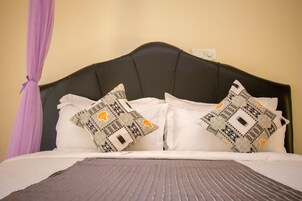 Una cama con cabecera negra, almohadas blancas y un cojín estampado.