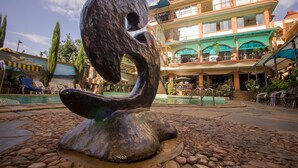 Escultura num pátio com piscina, um edifício com varandas e área de estar ao ar livre.