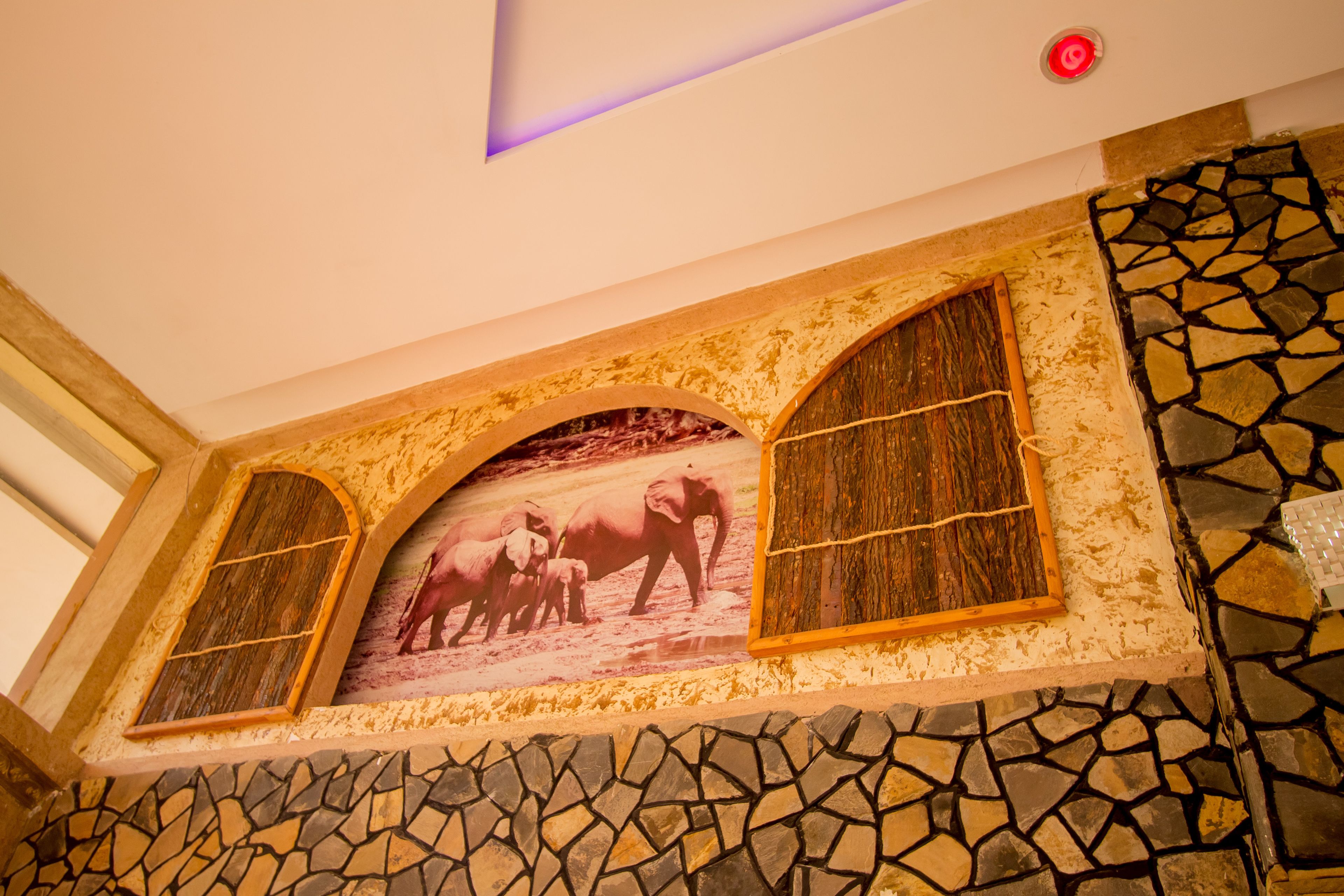 Una habitación con suelo de mosaico de piedra, un cuadro con marco de madera de elefantes y techo con luz púrpura.