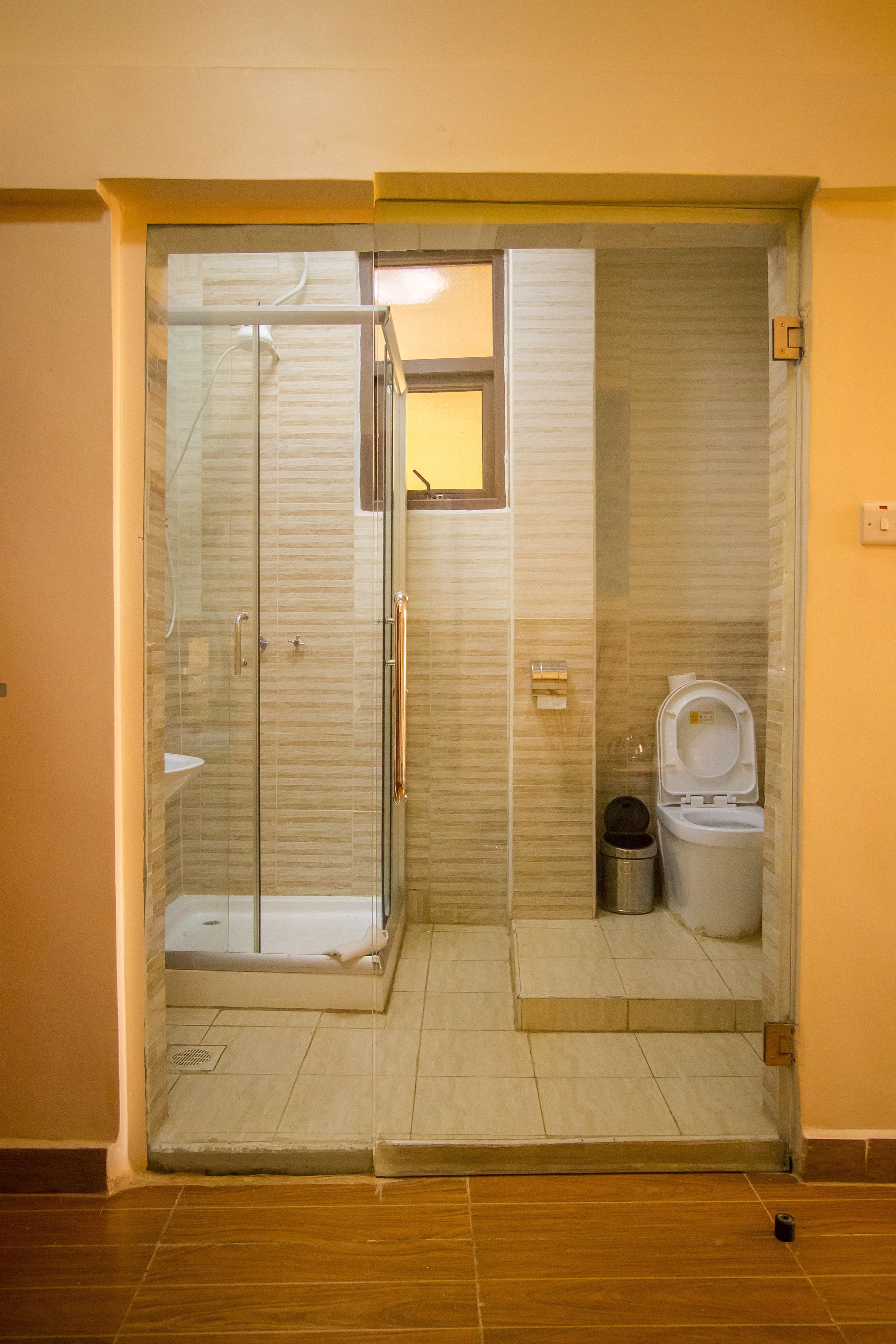 Un baño con cabina de ducha de vidrio, inodoro y una ventana pequeña.