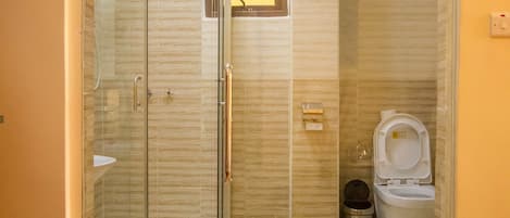 Un baño con cabina de ducha de vidrio, inodoro y una ventana pequeña.