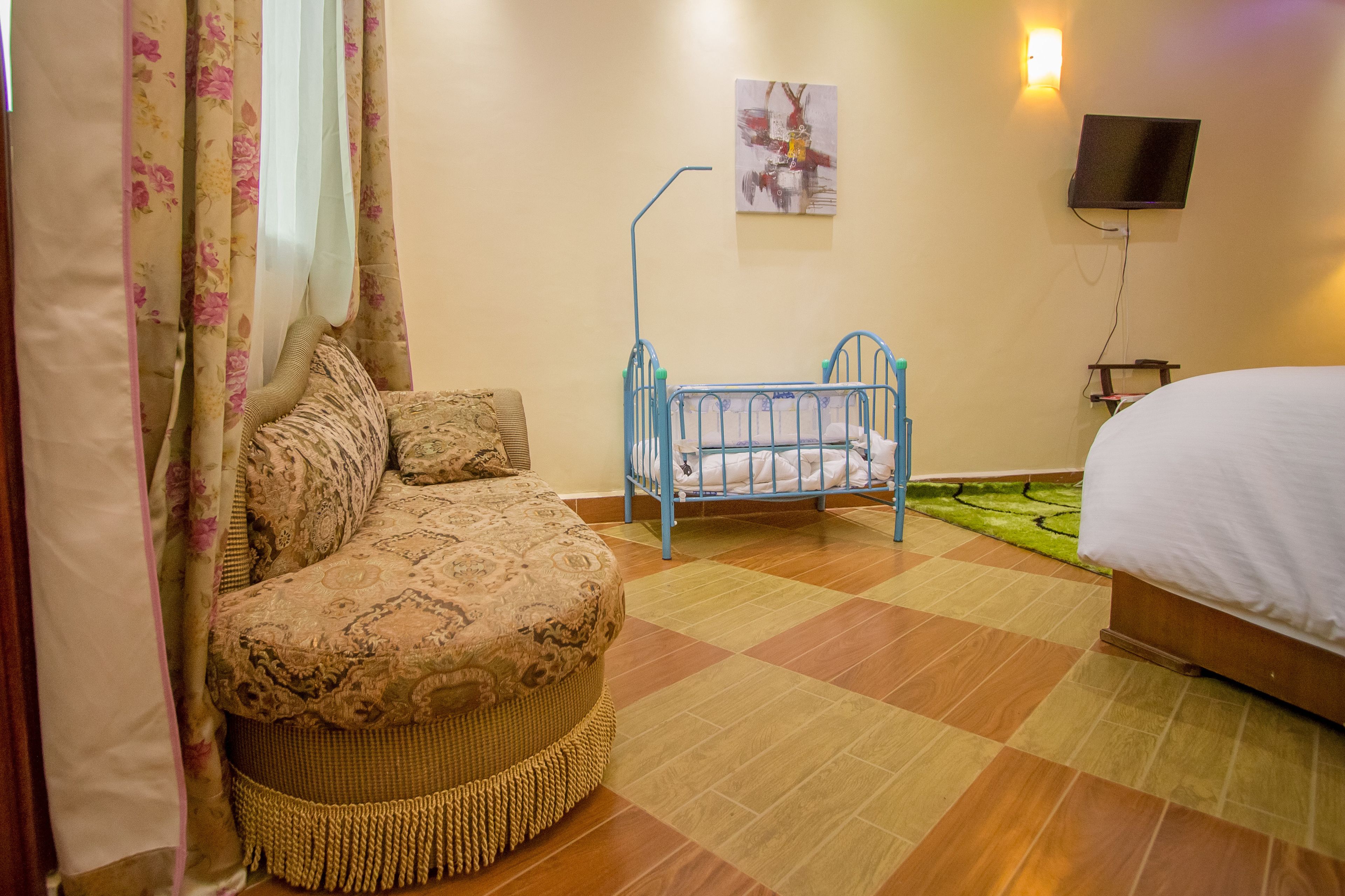 A bedroom with a bed, a crib, a sofa, a patterned rug, and a painting on the wall.
