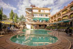 Un hotel de varios pisos con piscina, mobiliario exterior y balcones.