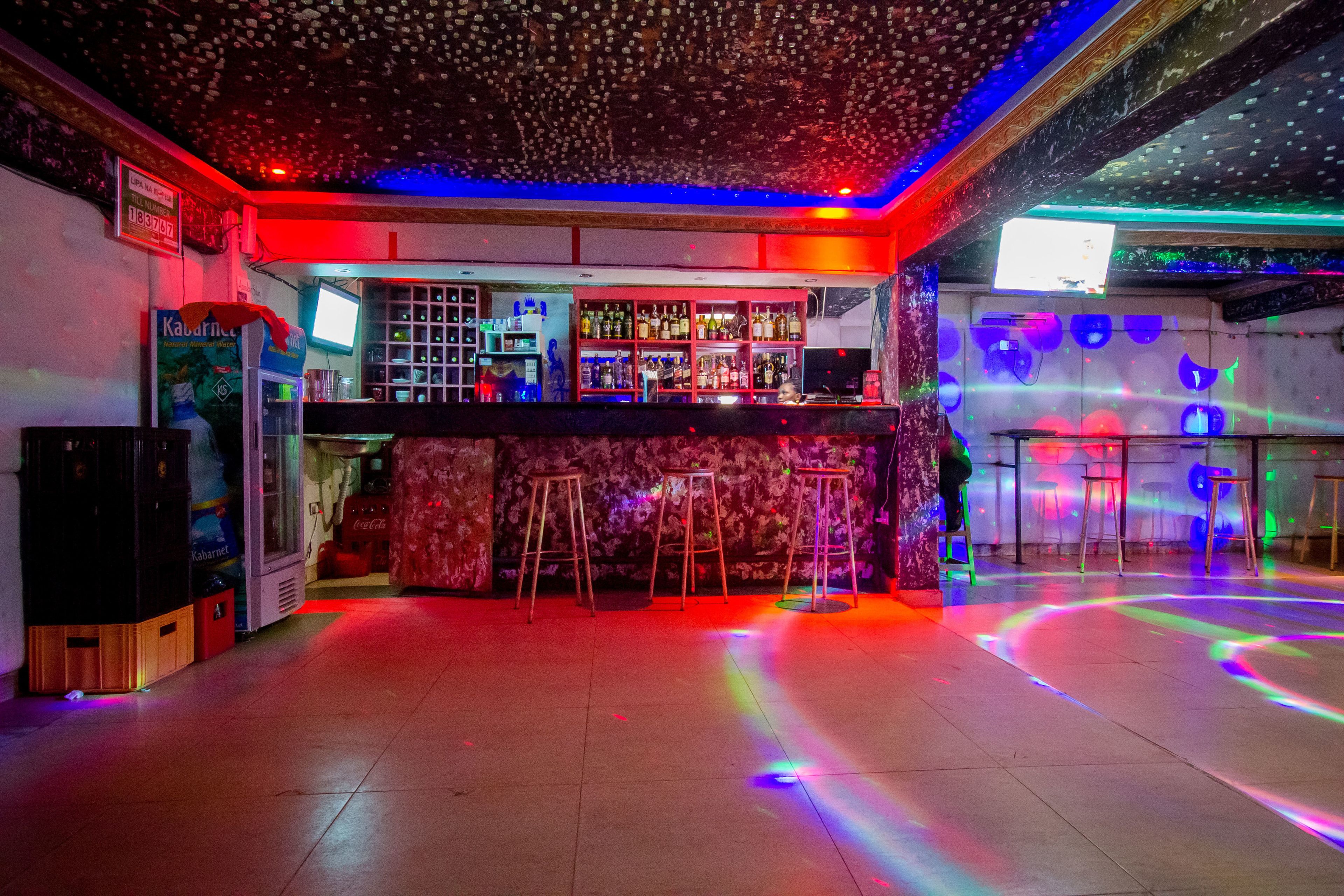 A bar area with stools, a bar counter, and shelves of bottles.