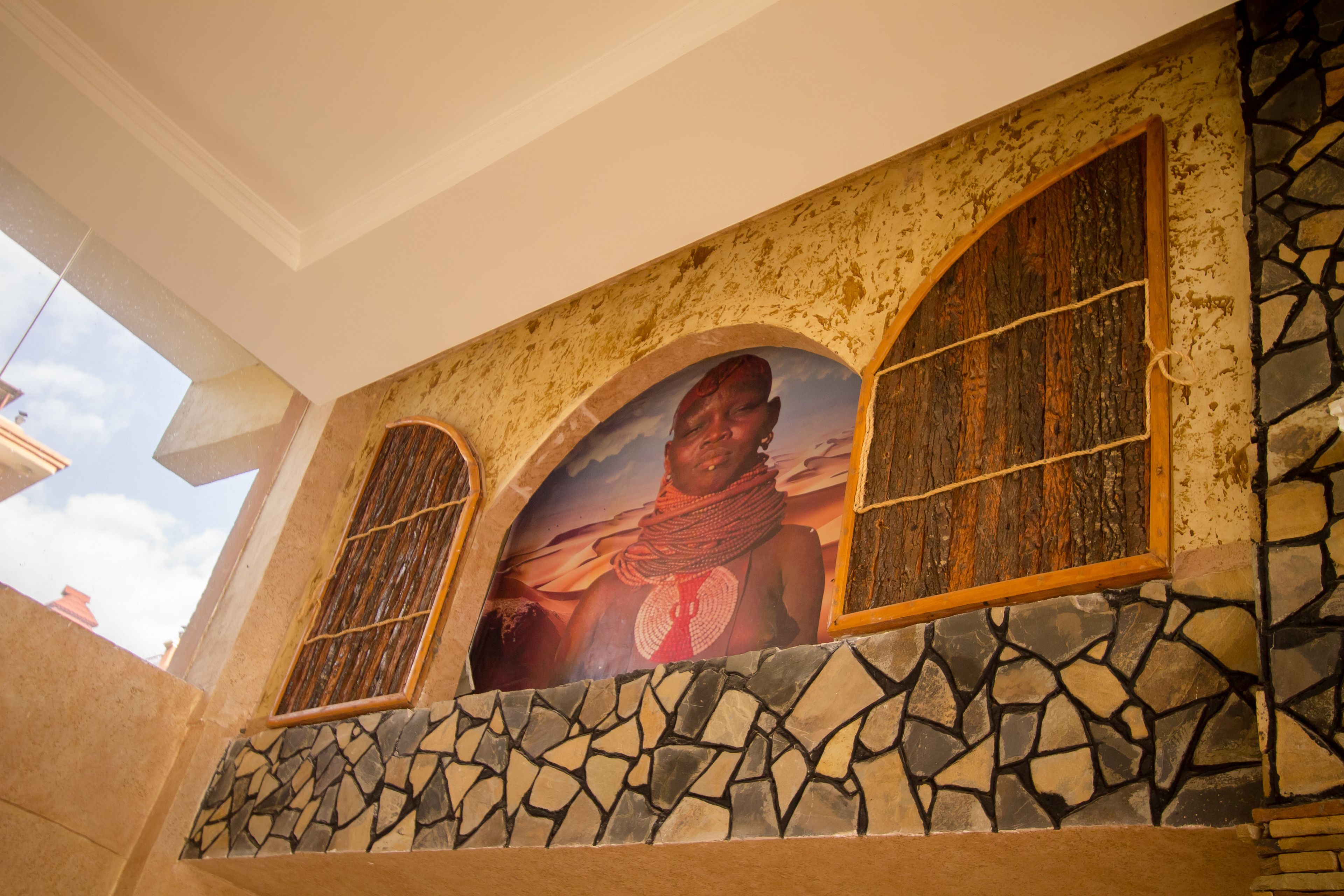 A building facade with a stone mosaic base, a large arched window with a framed picture, and a smaller window with a wooden lattice design.