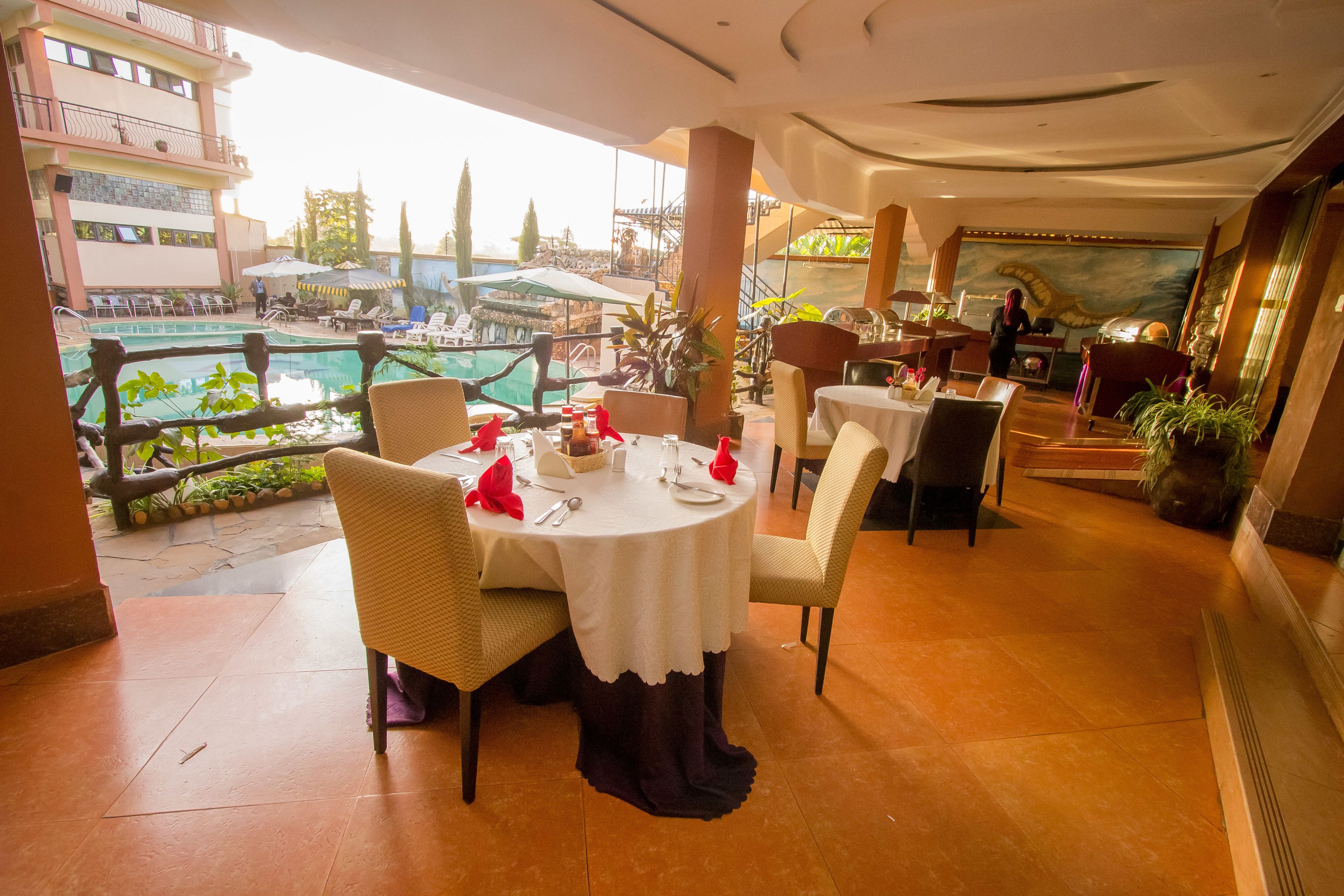 A restaurant with round tables, chairs, and a view of a pool and buildings.