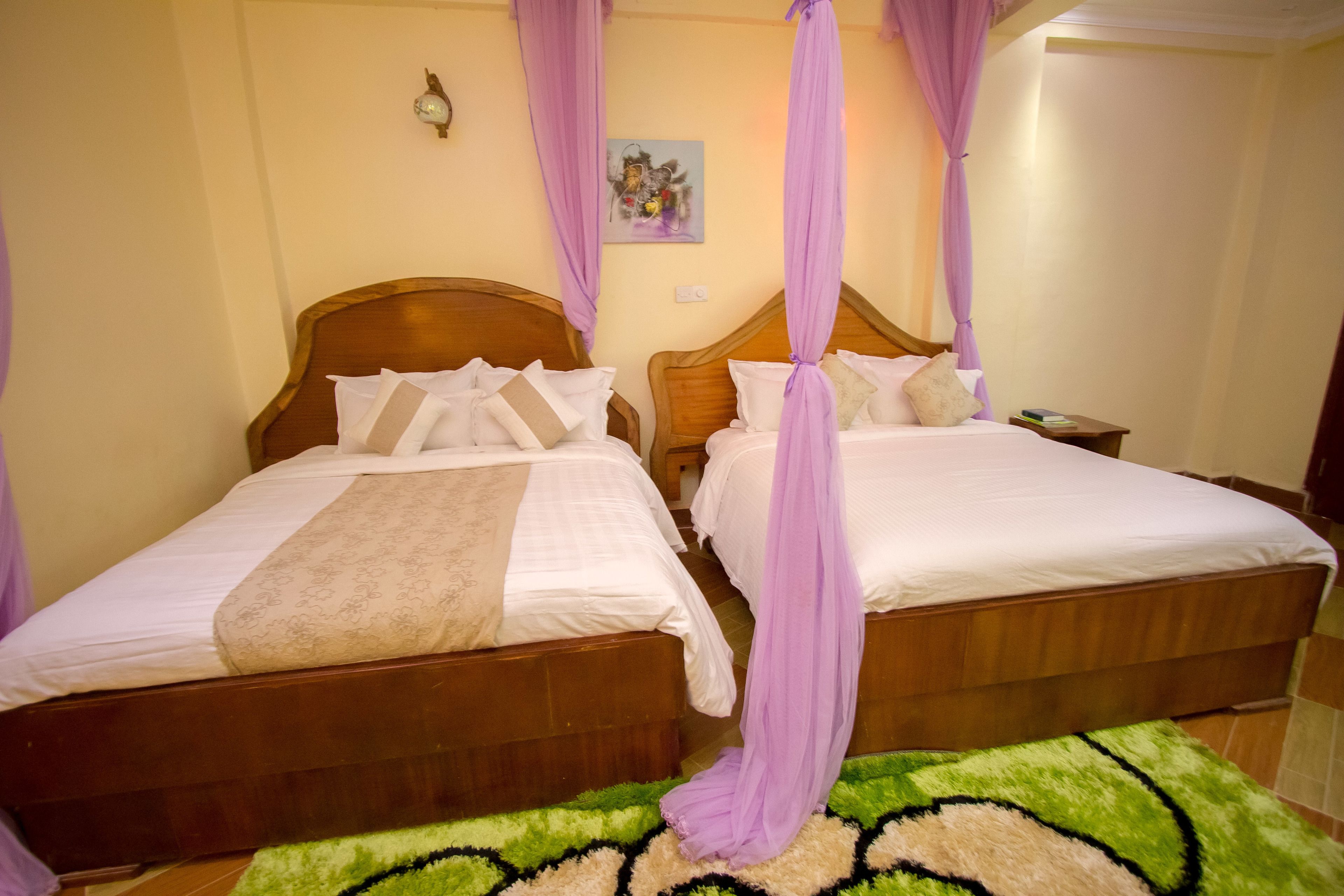 Two wooden beds with white linens and purple canopy drapes.
