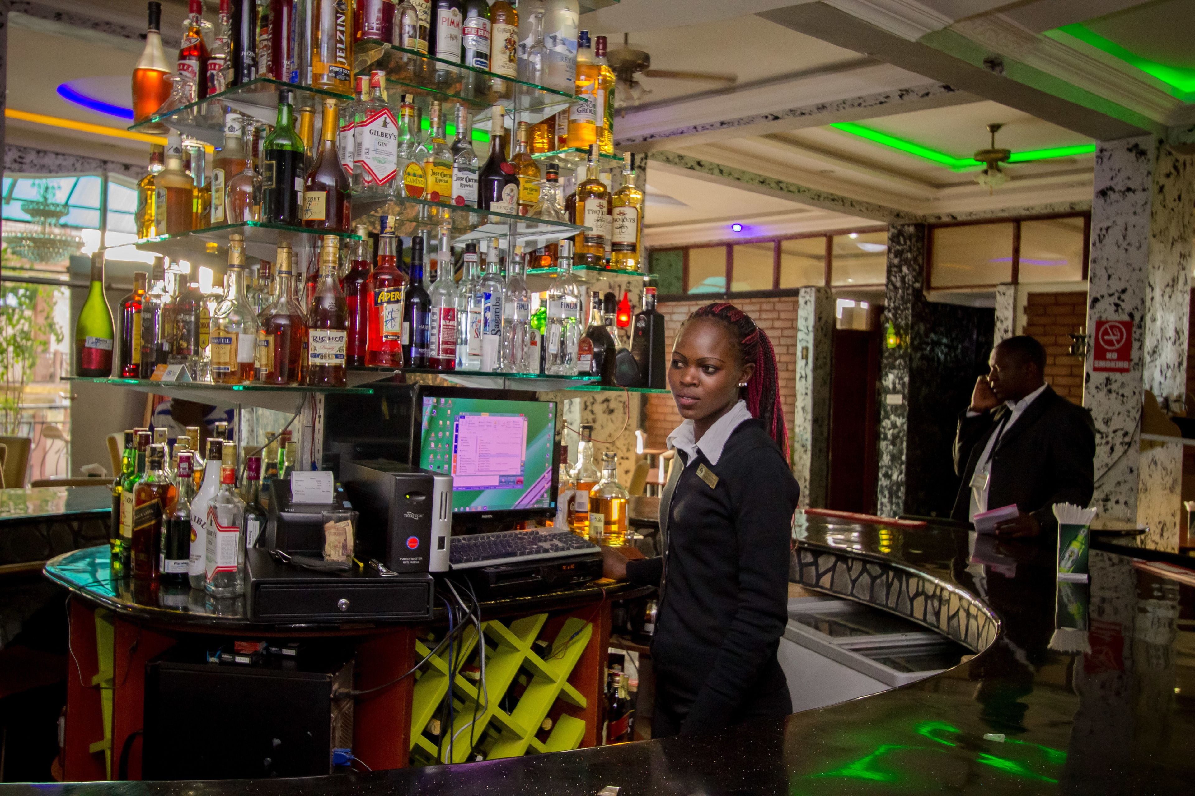 A bar area with shelves of liquor bottles, a computer, and a cash register.