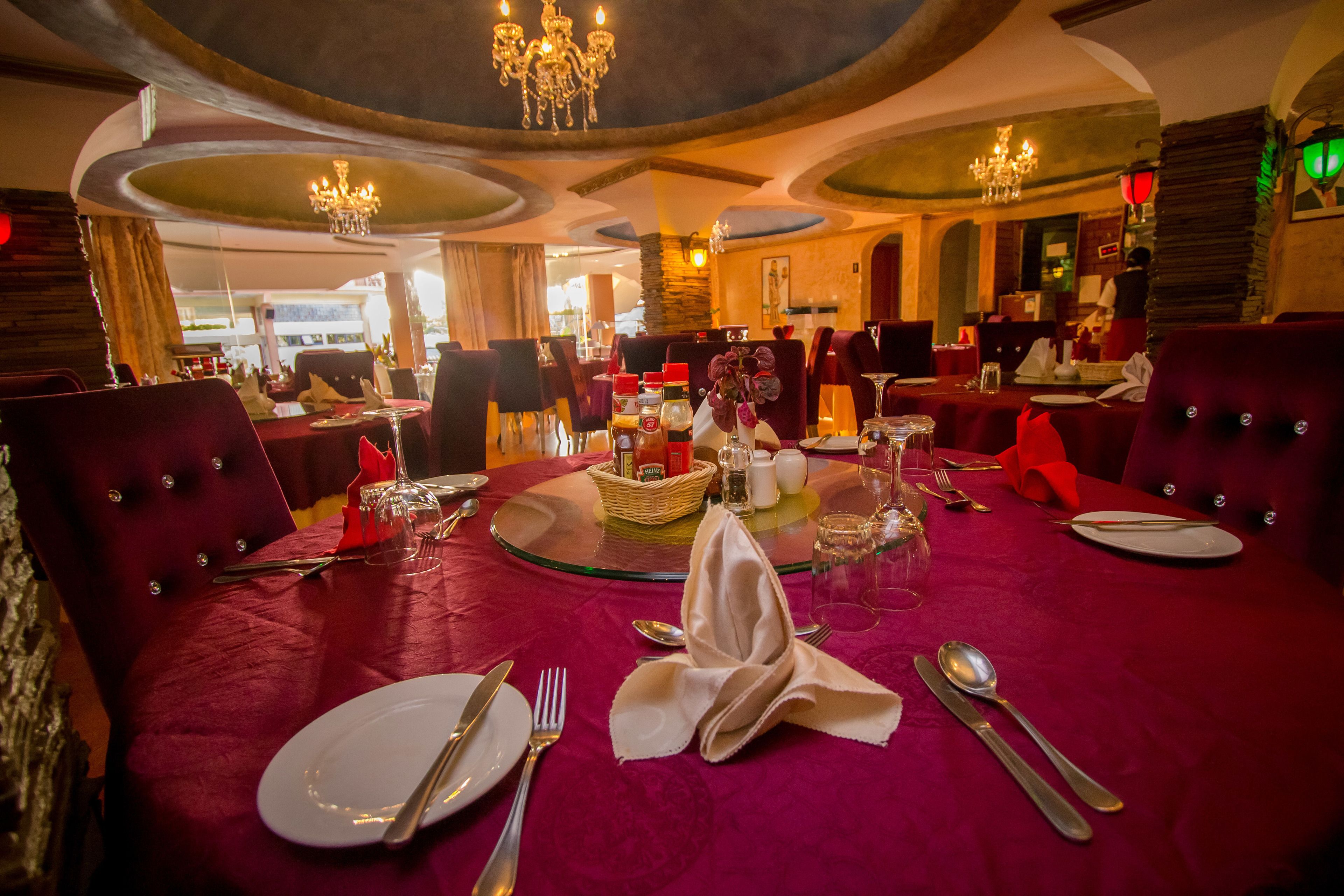 A dining area with round tables set for four, each with a red tablecloth, silverware, and a folded napkin.