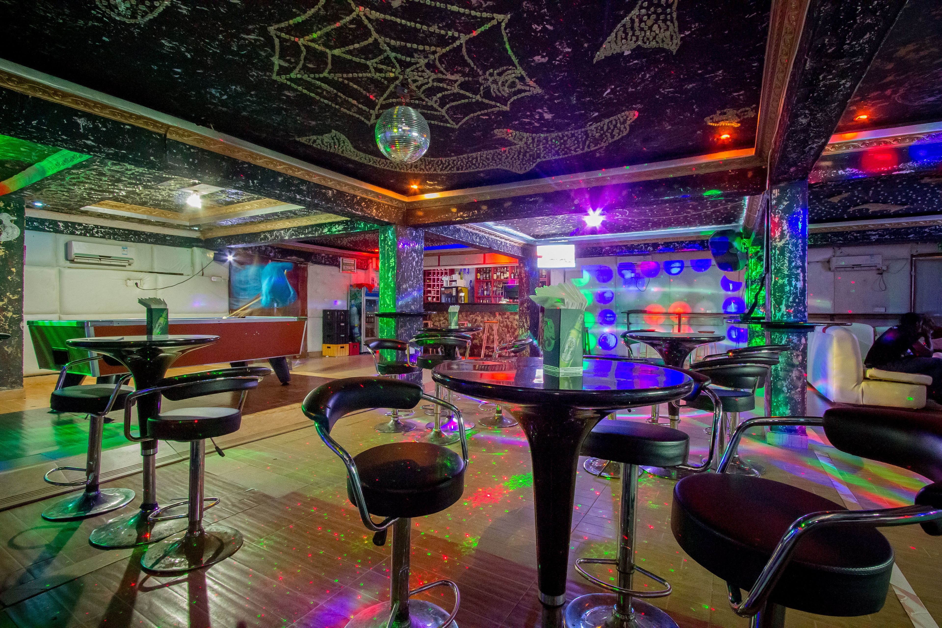 Una zona de bar con varios taburetes, una bola de discoteca y una barra.