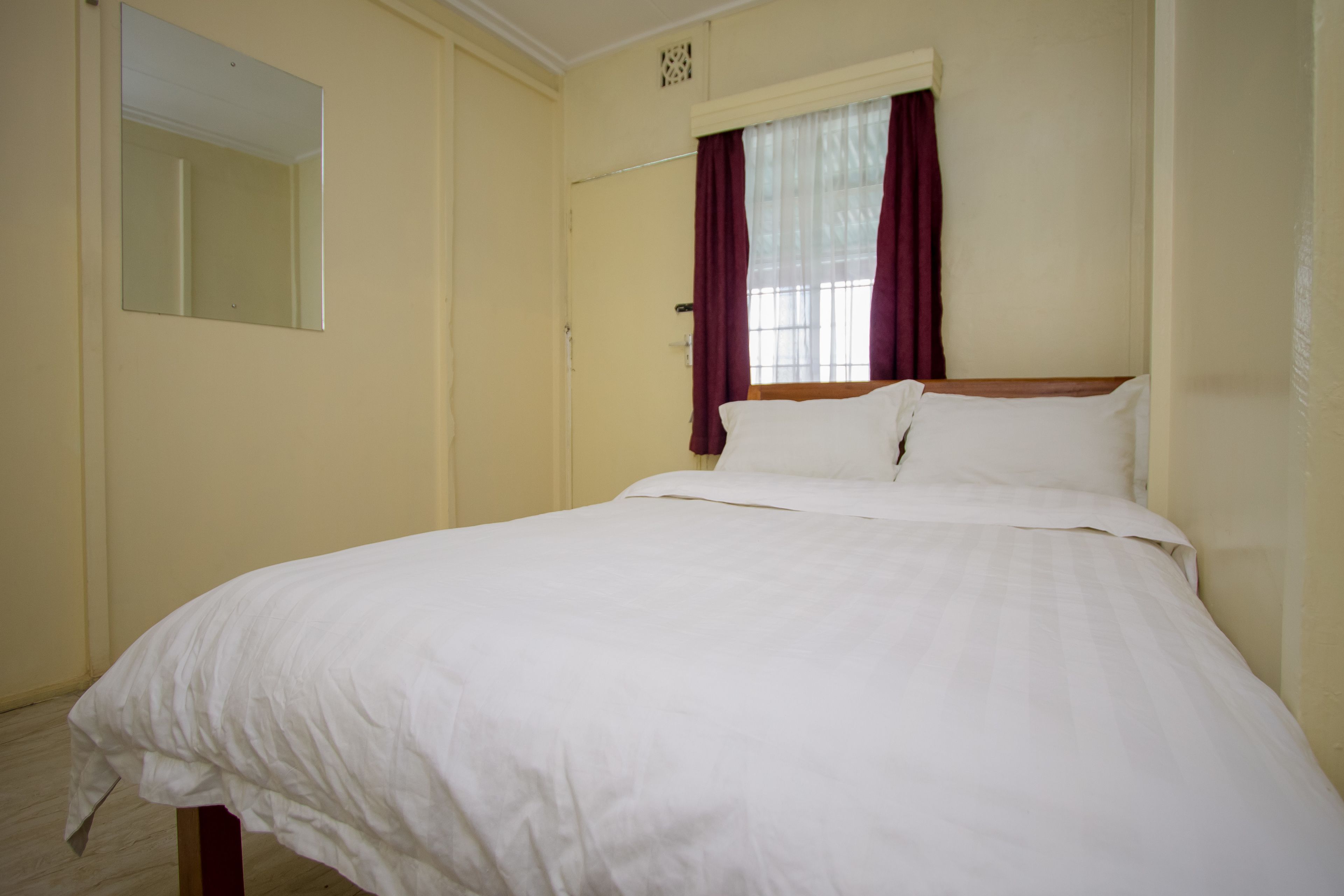 A bedroom with a single bed, a window with curtains, and a mirror on the wall.