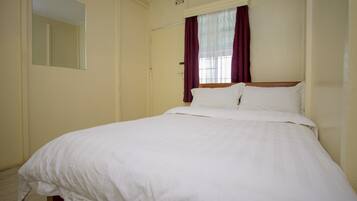 A bedroom with a single bed, a window with curtains, and a mirror on the wall.