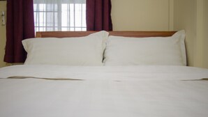 A bed with white linens, a wooden headboard, and red curtains. - Balis Best Bar and Resort (Nairobi)