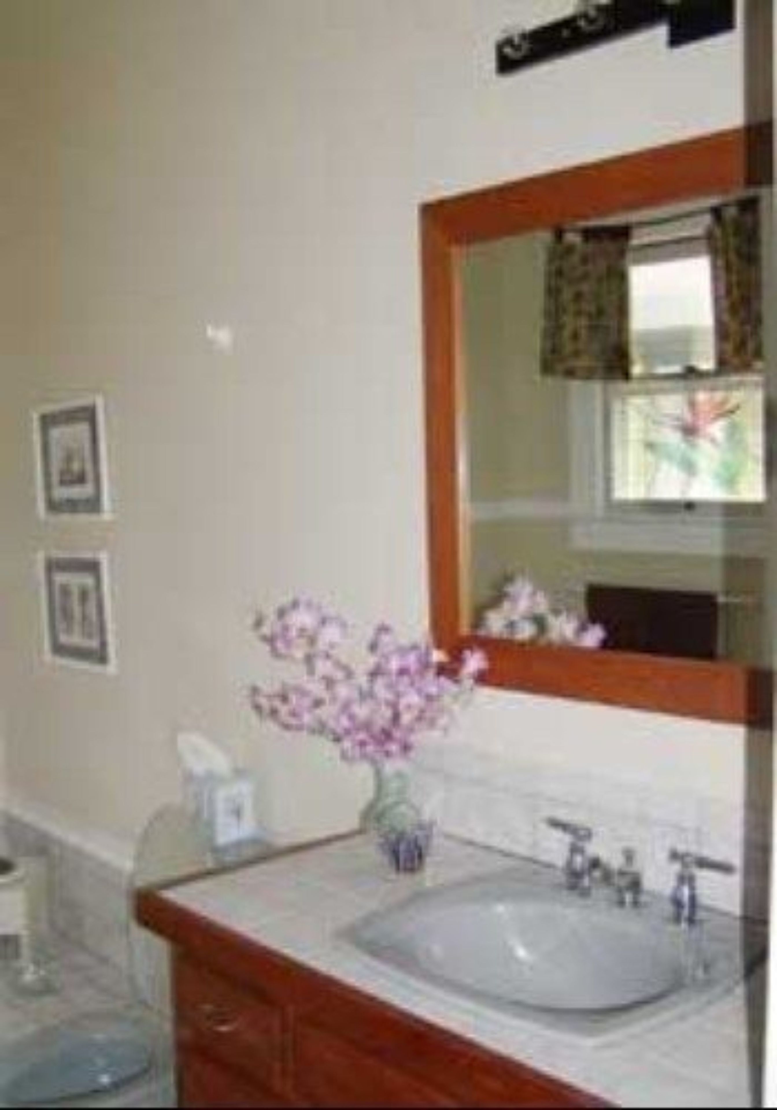 Une salle de bain avec un grand miroir, un lavabo et un vase rempli de fleurs.