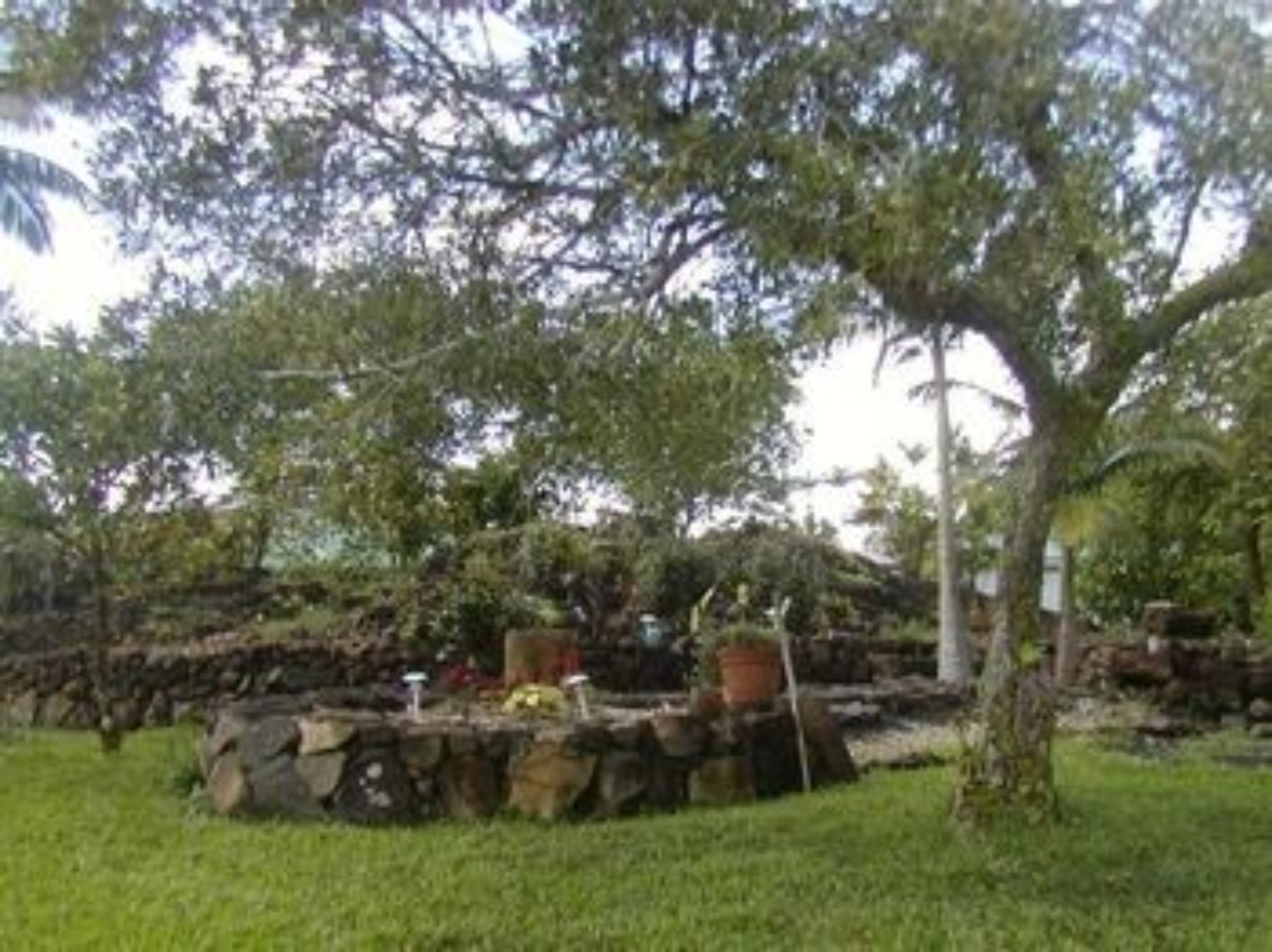 A stone structure with a small garden area, surrounded by trees and grass.