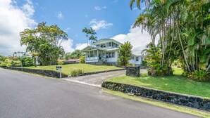A two-story house with a porch, surrounded by tropical vegetation and a stone wall. - Old Hawaiian B and B (Hilo)