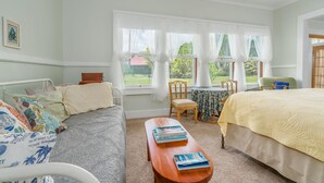 A bedroom with a bed, a sofa, a small table, and a window with curtains. - Old Hawaiian B and B (Hilo)