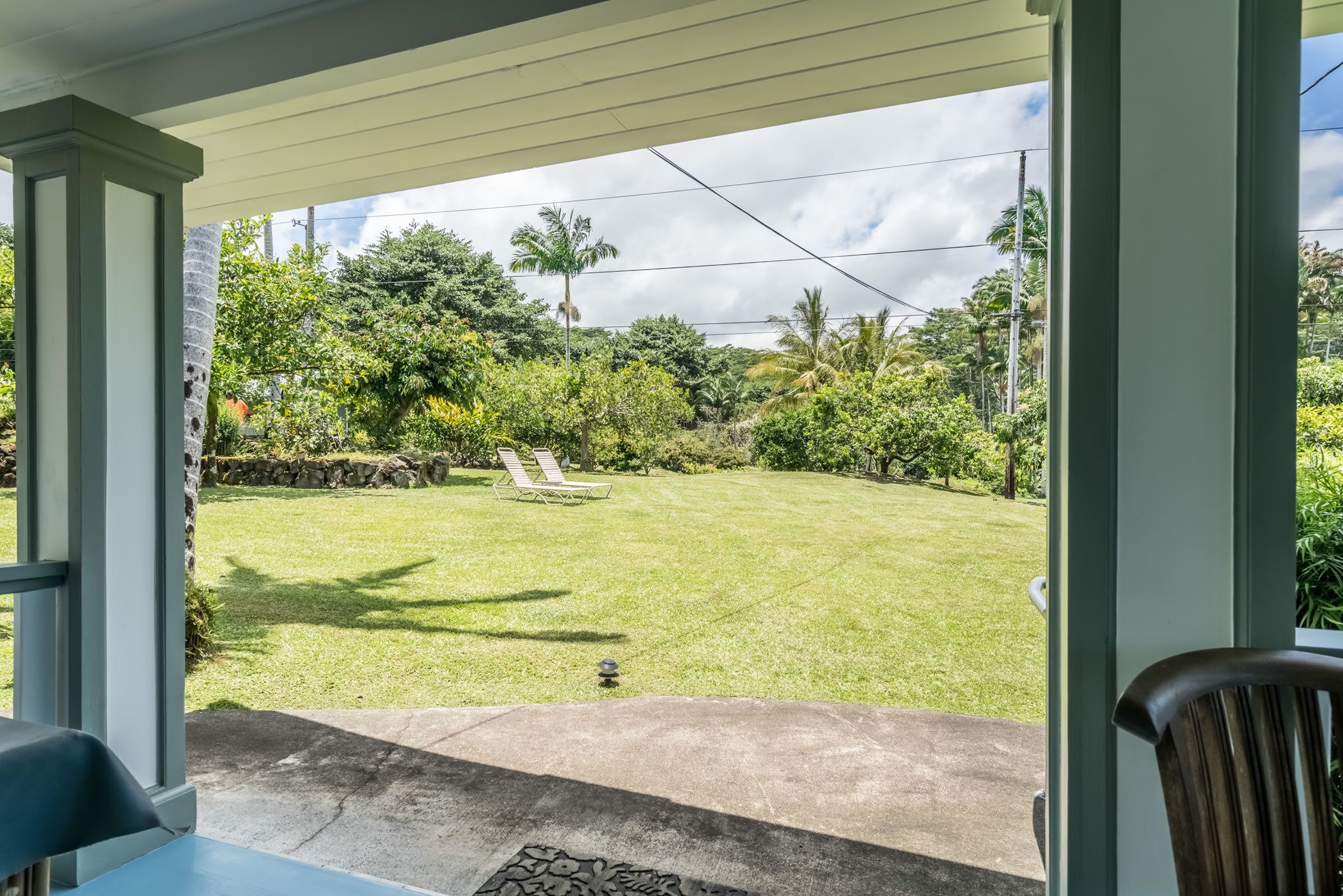 A covered patio area with a view of a well-maintained lawn and a few lounge chairs.